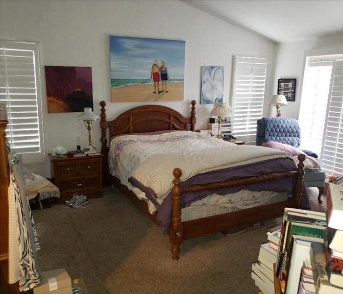 A furnished bedroom with a picture hanging on the wall. Books and knick-knacks around the room