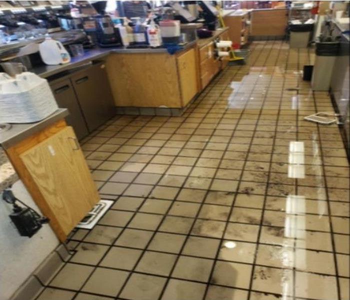 A restaurant kitchen with brown cabinets and white tile filled with dirty water everywher..