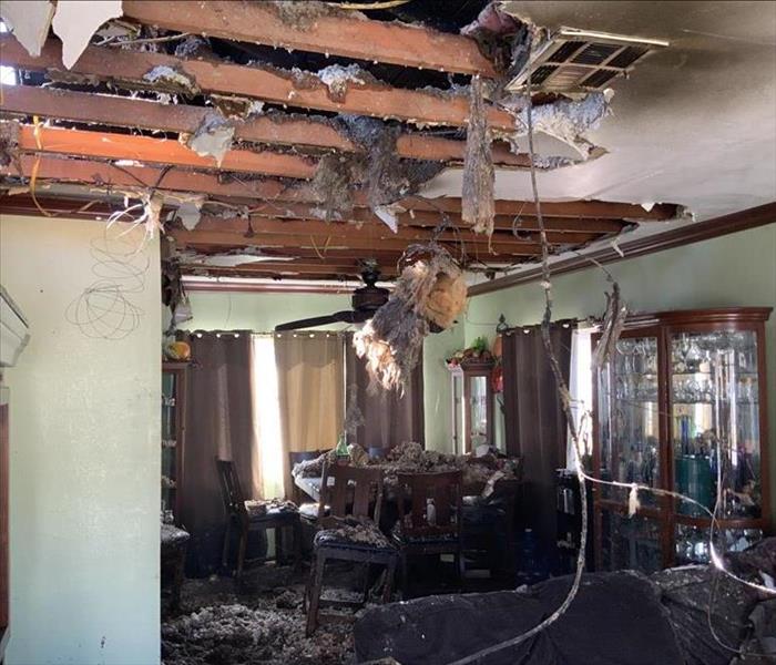 A living room with furniture filled with soot and fire damage. The ceiling drywall falling with insulation coming out of it. 