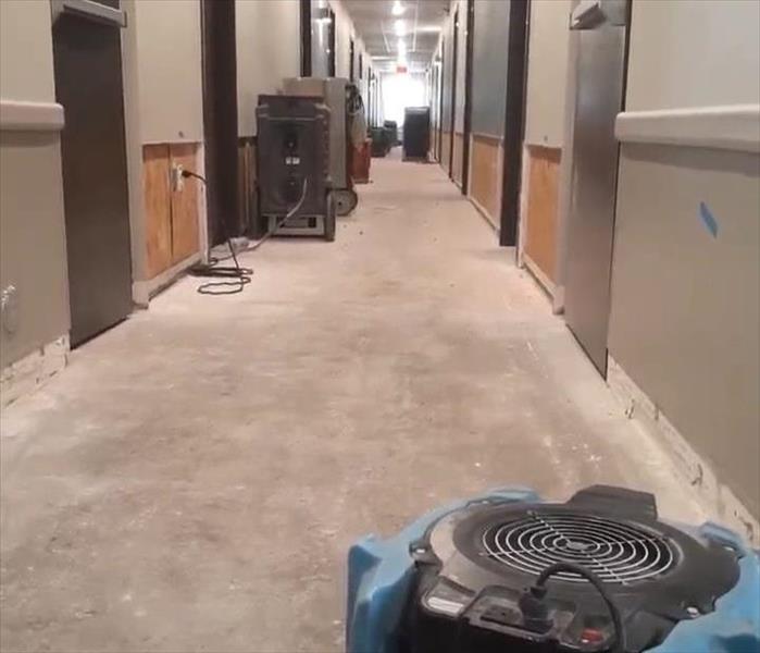 Air dryers sitting in the hallway of a hotel. Hallway has some drywall and floor missing. 