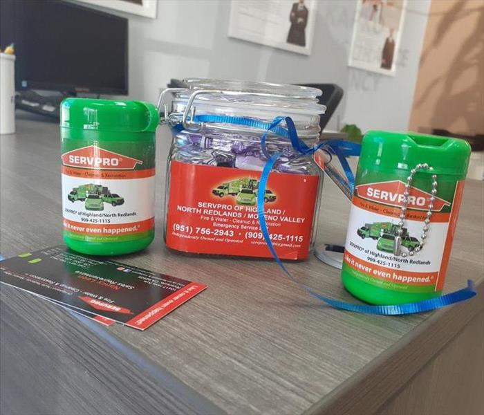 Candy jar, 2 green canisters and business cards on a office desk displaying our SERVPRO logo. 