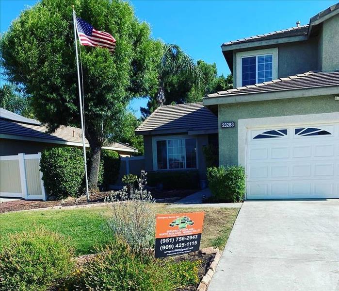 Front of a 2 story home with a American Flag Standing tall. on the lawn is our SERVPRO sign. 
