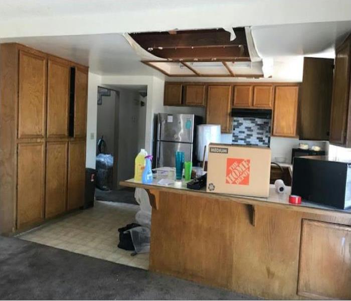 A kitchen with brown cabinets and kitchen essentials. The ceiling in the kitchen has a open whole showing there was damage. 